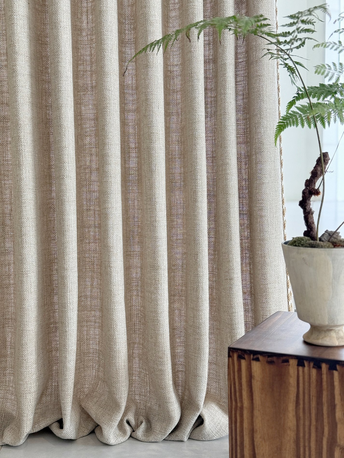 Neutral curtain panel with refined side trim beside a plant